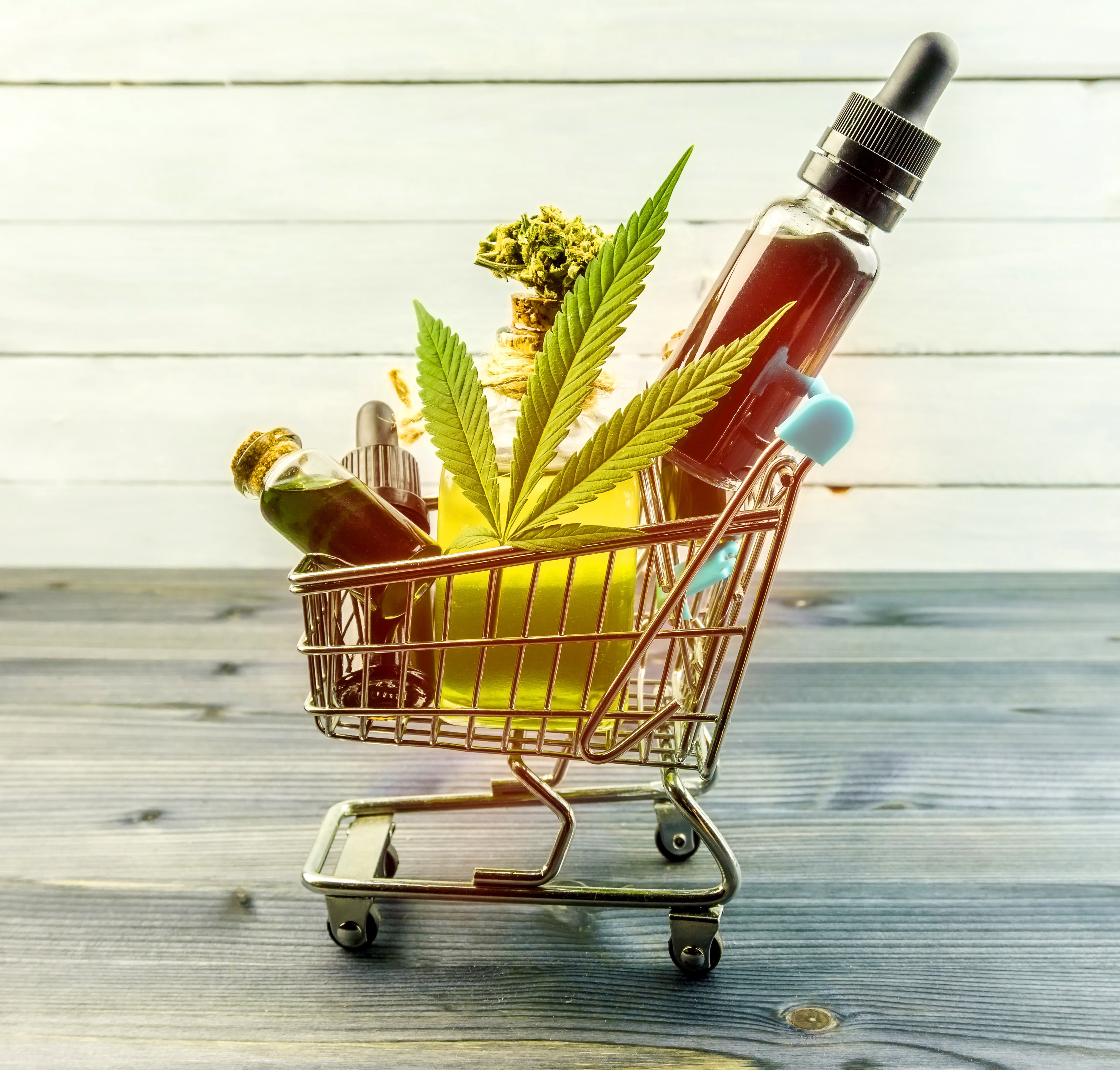 A shopping cart filled with cannabis concentrates, oils, and the plant, rolls across a wooden table.