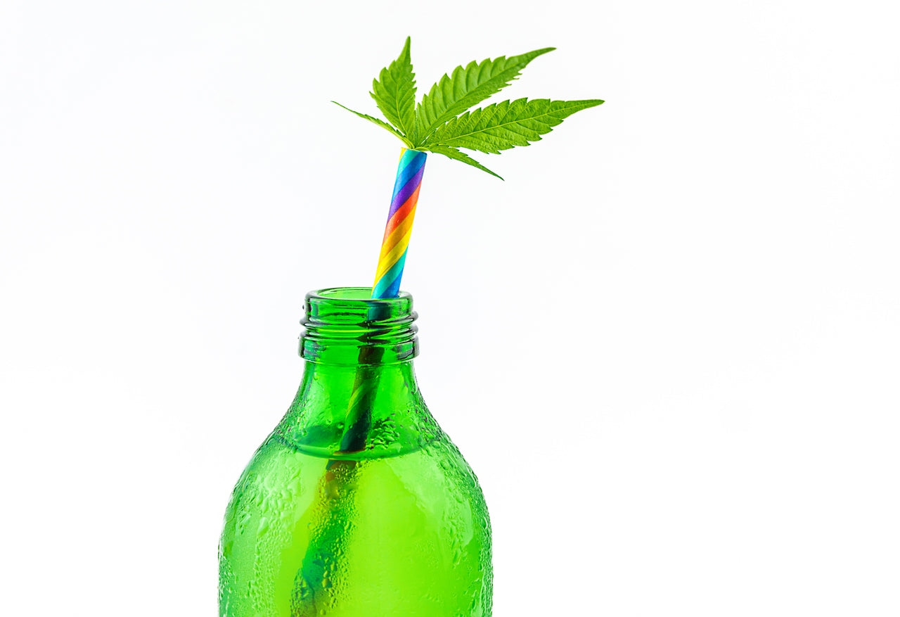 A cannabis infused beverage in a green bottle has a rainbow straw with a cannabis leaf coming out of it.