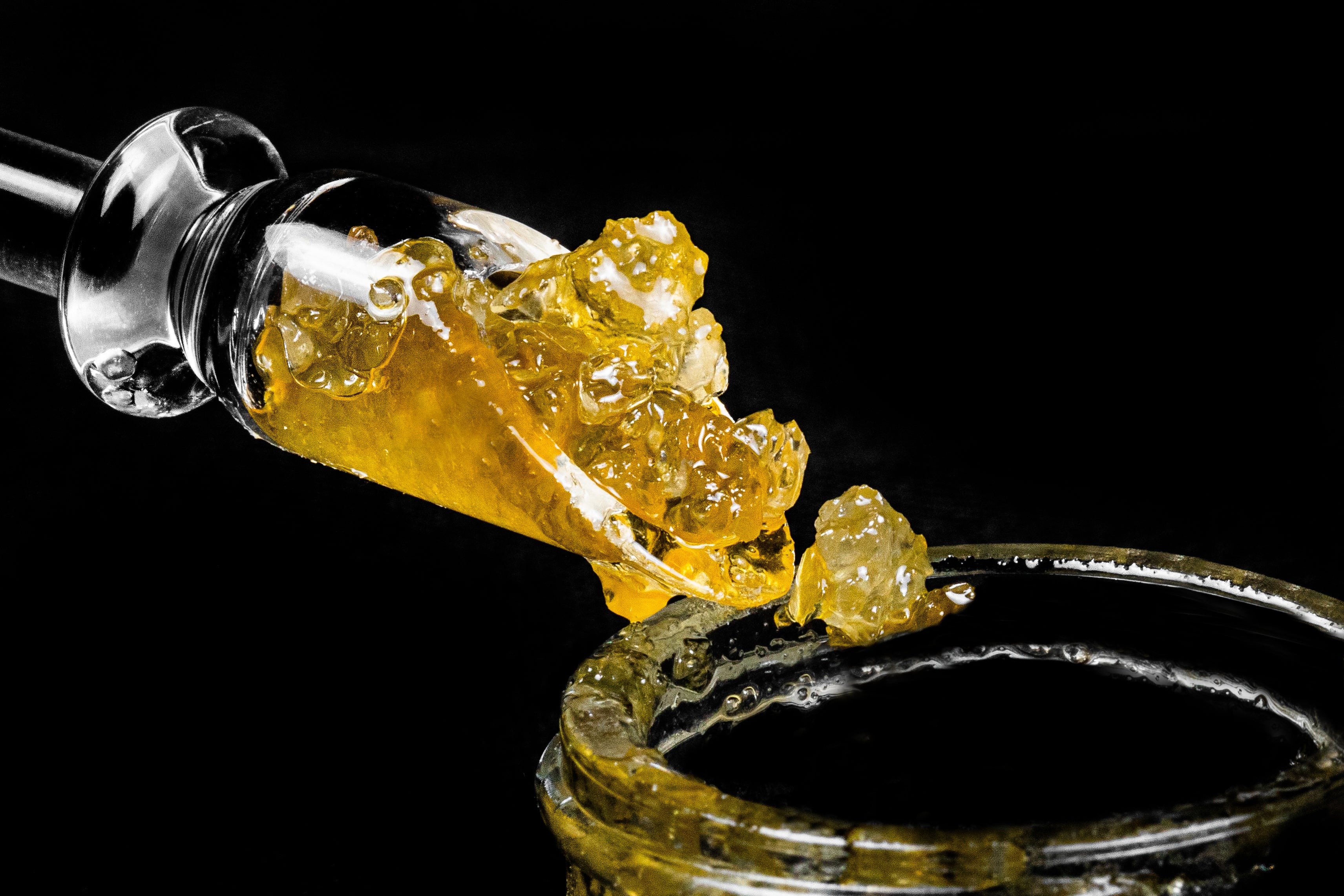 Live resin diamonds are scooped out of a glass jar with a glass dabbing tool.
