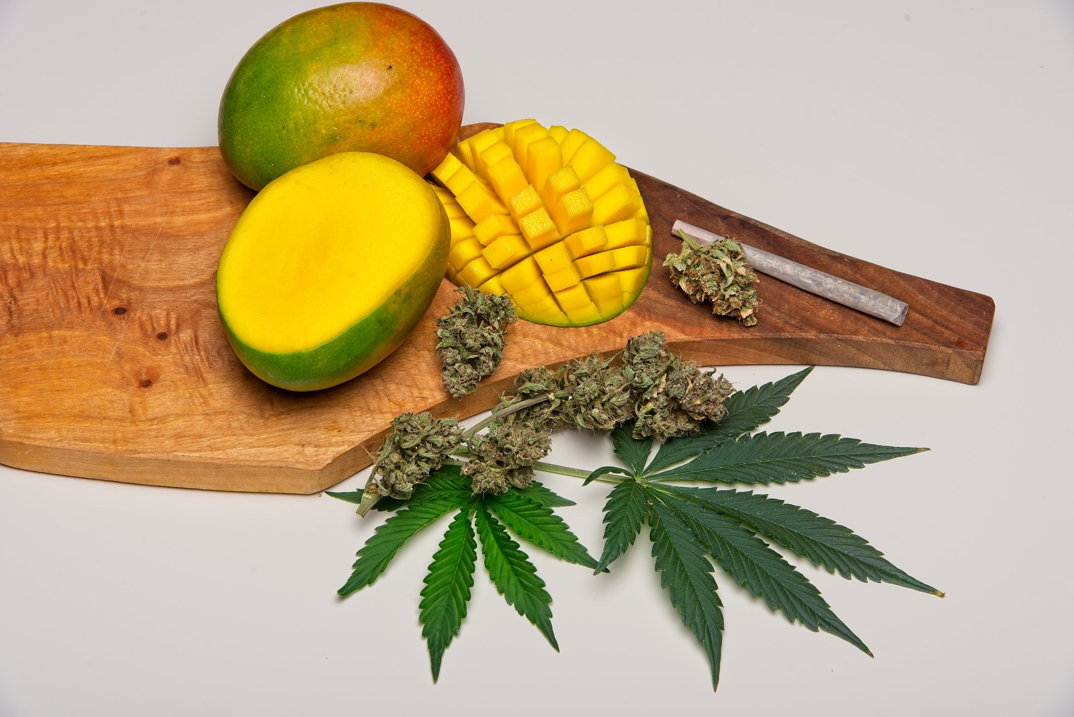 On a wooden cutting board, a cut-up mango sits next to cannabis flower, which can also have the terpene myrcene.