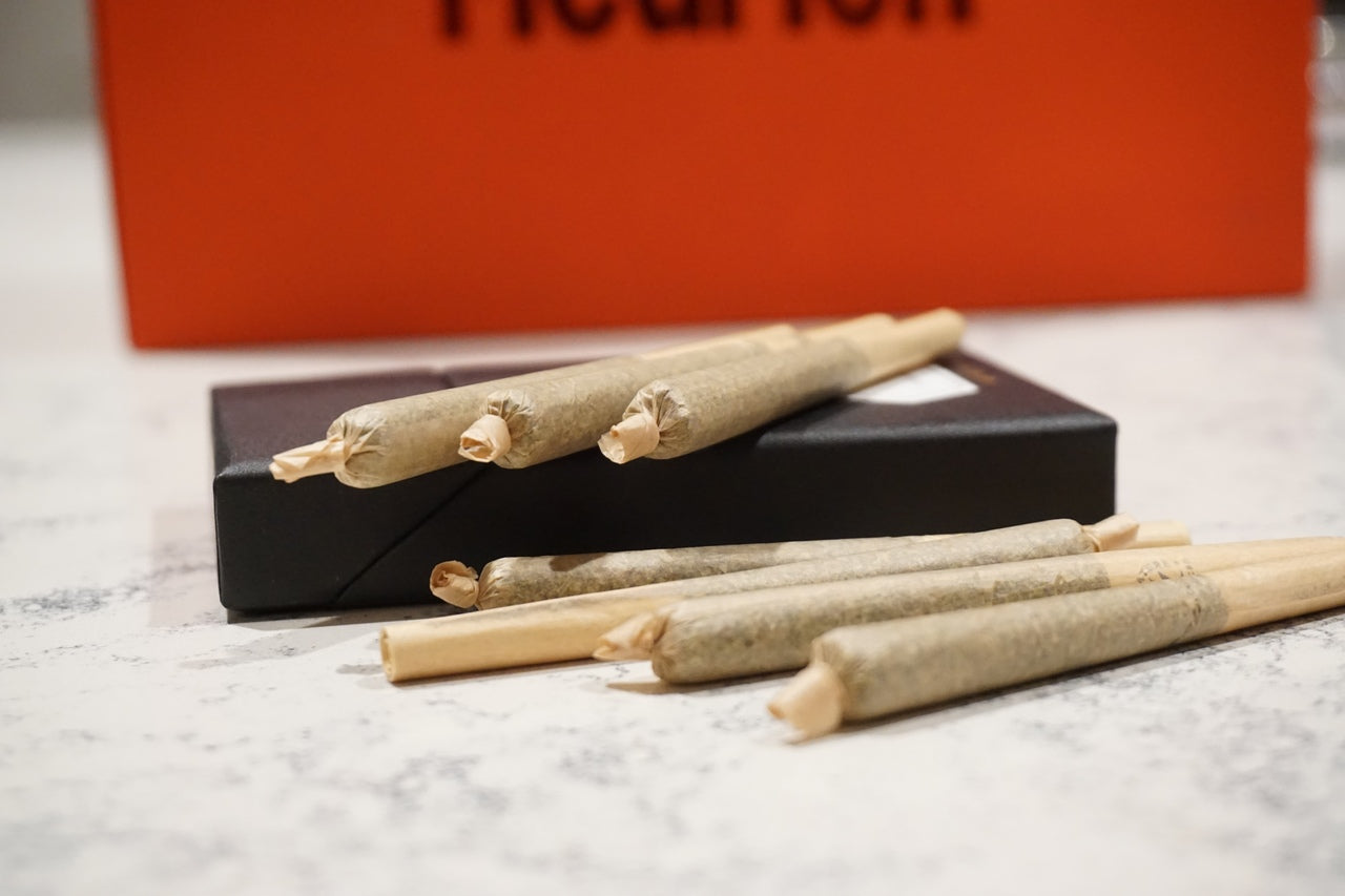 Three cannabis pre-rolls lie ontop of and next to their black package.