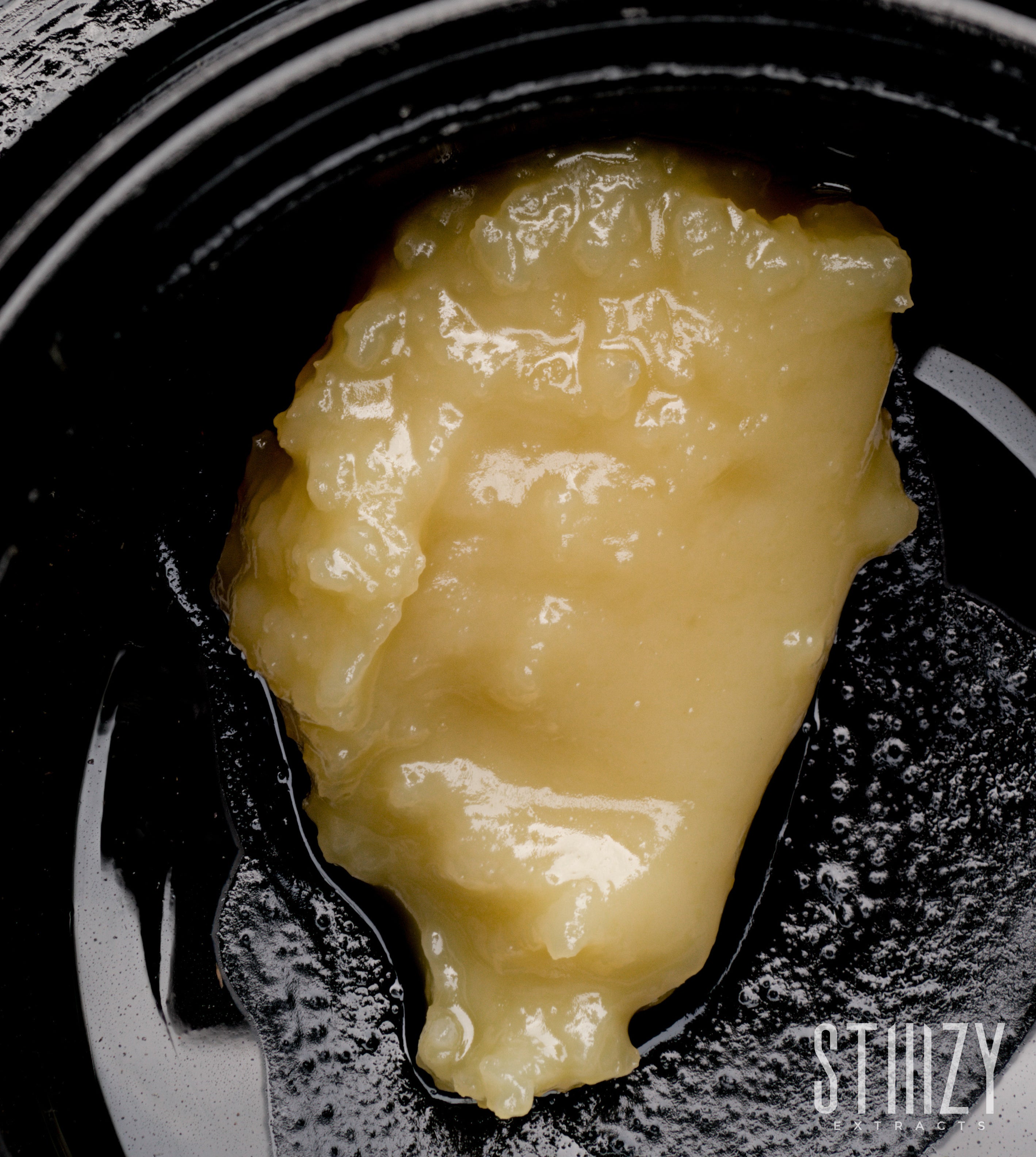 A golden glob of live rosin badder sits in a black STIIIZY jar.