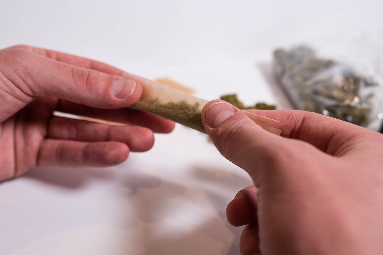 Ground cannabis flower is being rolled up into a joint on a white surface.
