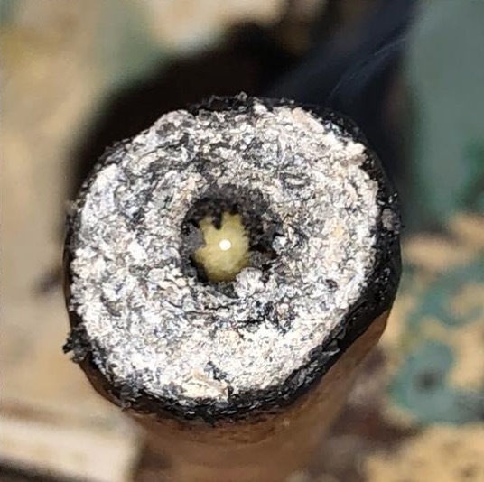 A hash hole with a live rosin extract shaped like a worm is being smoked and shown from the front.