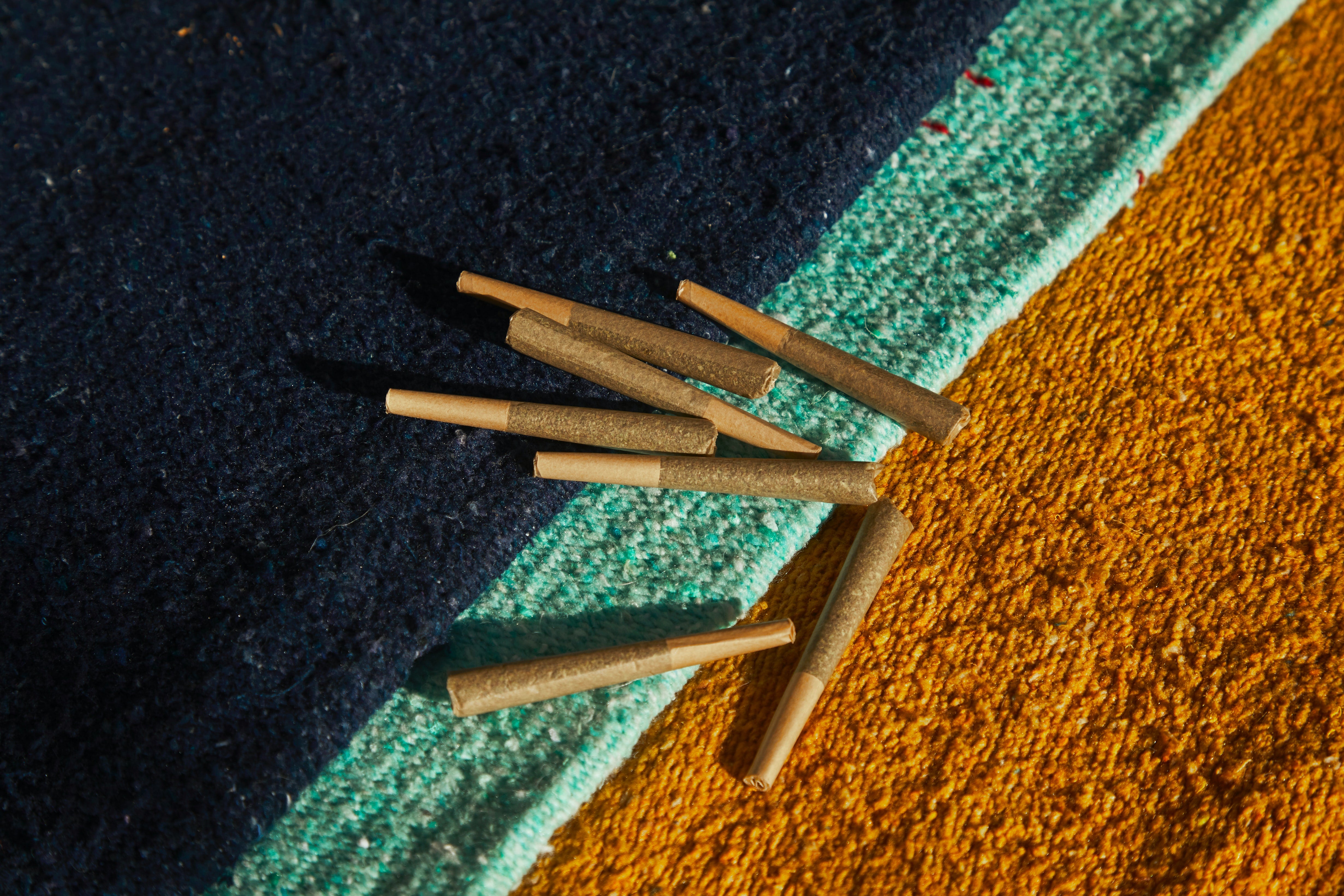 A cluster of infused pre-rolls are laid out on a beige, turquoise, and blue cloth.