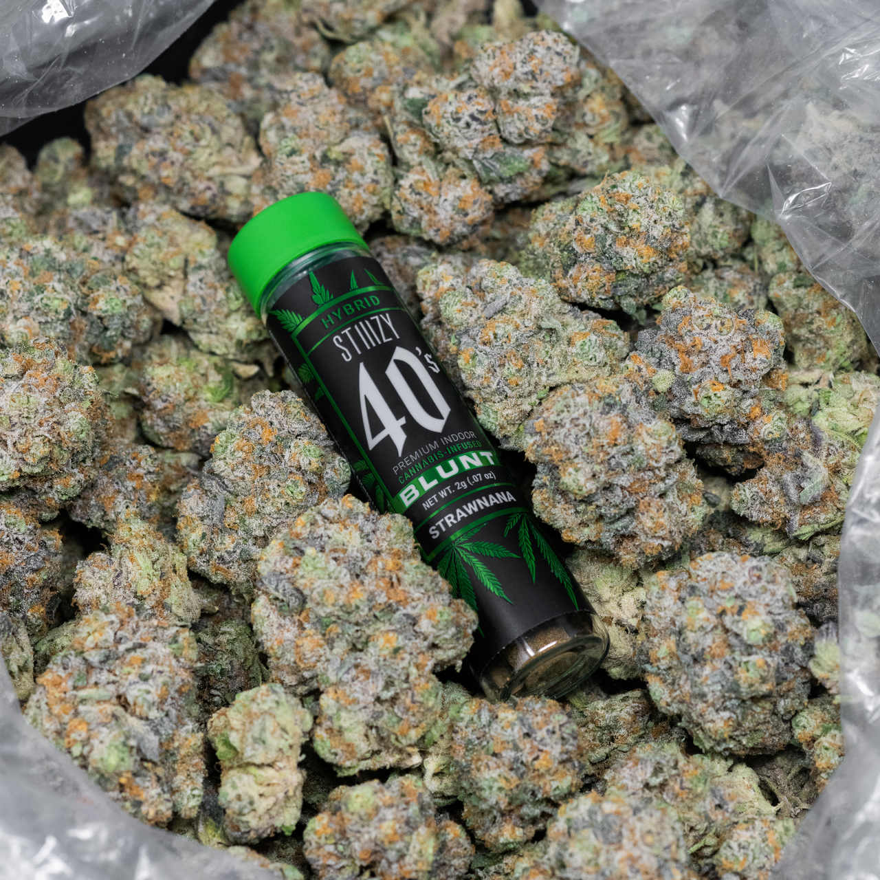 A jar with a green cap and a pre-roll blunt of hybrid cannabis flower sits in a pool of nugs.