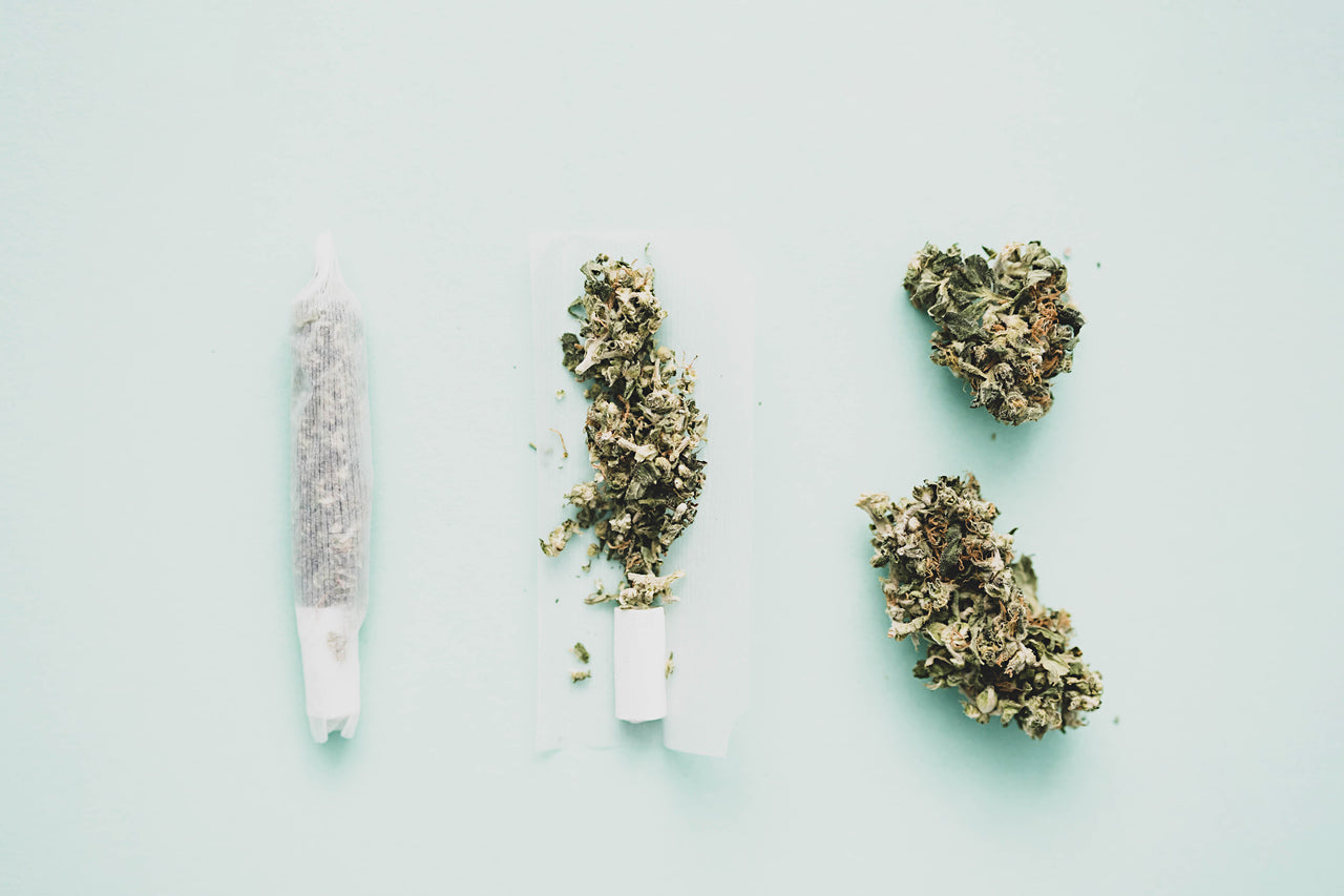 Two cannabis flower nugs sit next to a joint being rolled and a joint already rolled.