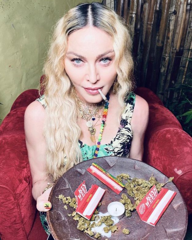 Madonna smokes a joint while holding up a plate with cannabis flower and rolling papers.