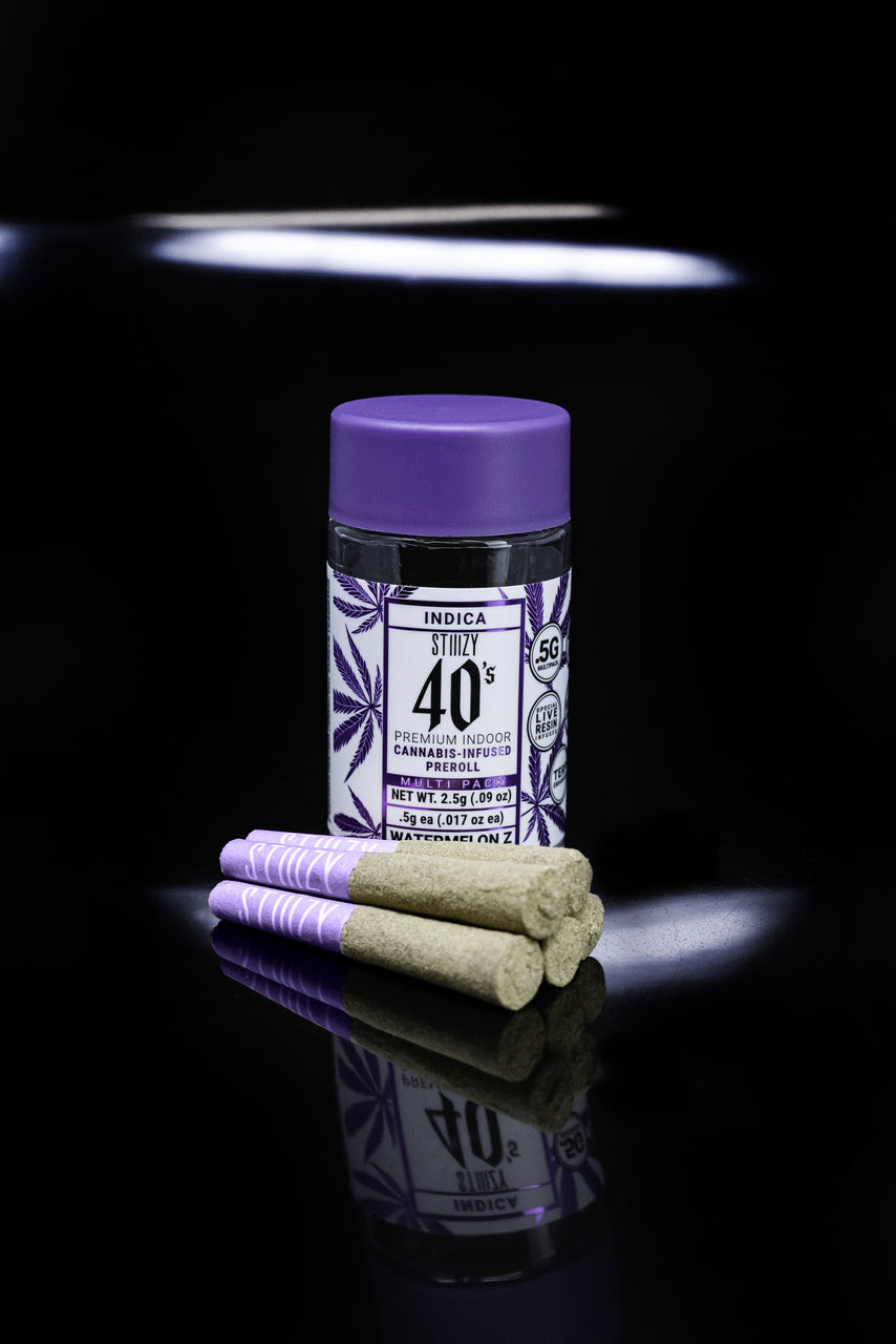 A multipack of infused indica cannabis pre-rolls stands on a black surface.