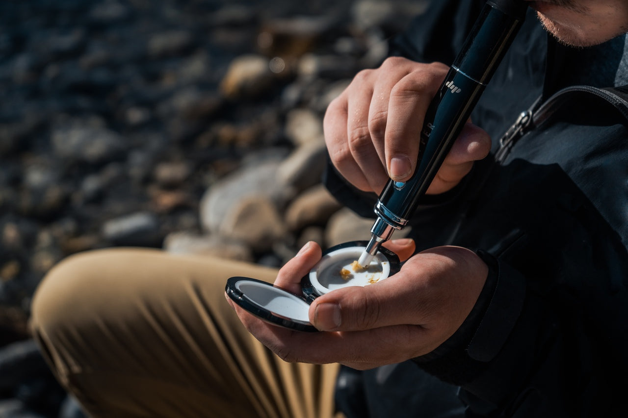 A person uses a black dab pen to dab a cannabis extract in a black and white case.