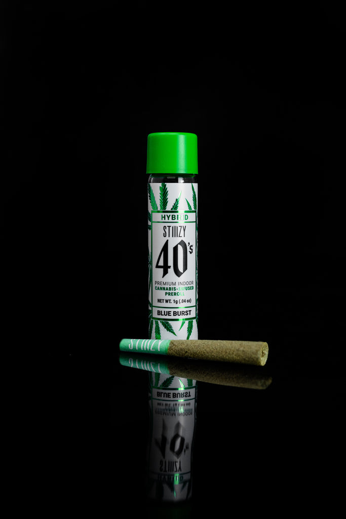 A pre-roll of cannabis flower lies on a black surface next to its container with a green cap.