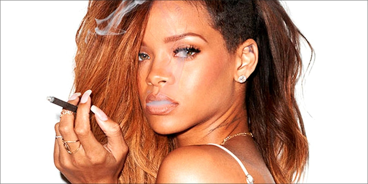 A well-known celebrity, Rihanna smokes cannabis flower in a blunt and wears rings, earrings, and a necklace.