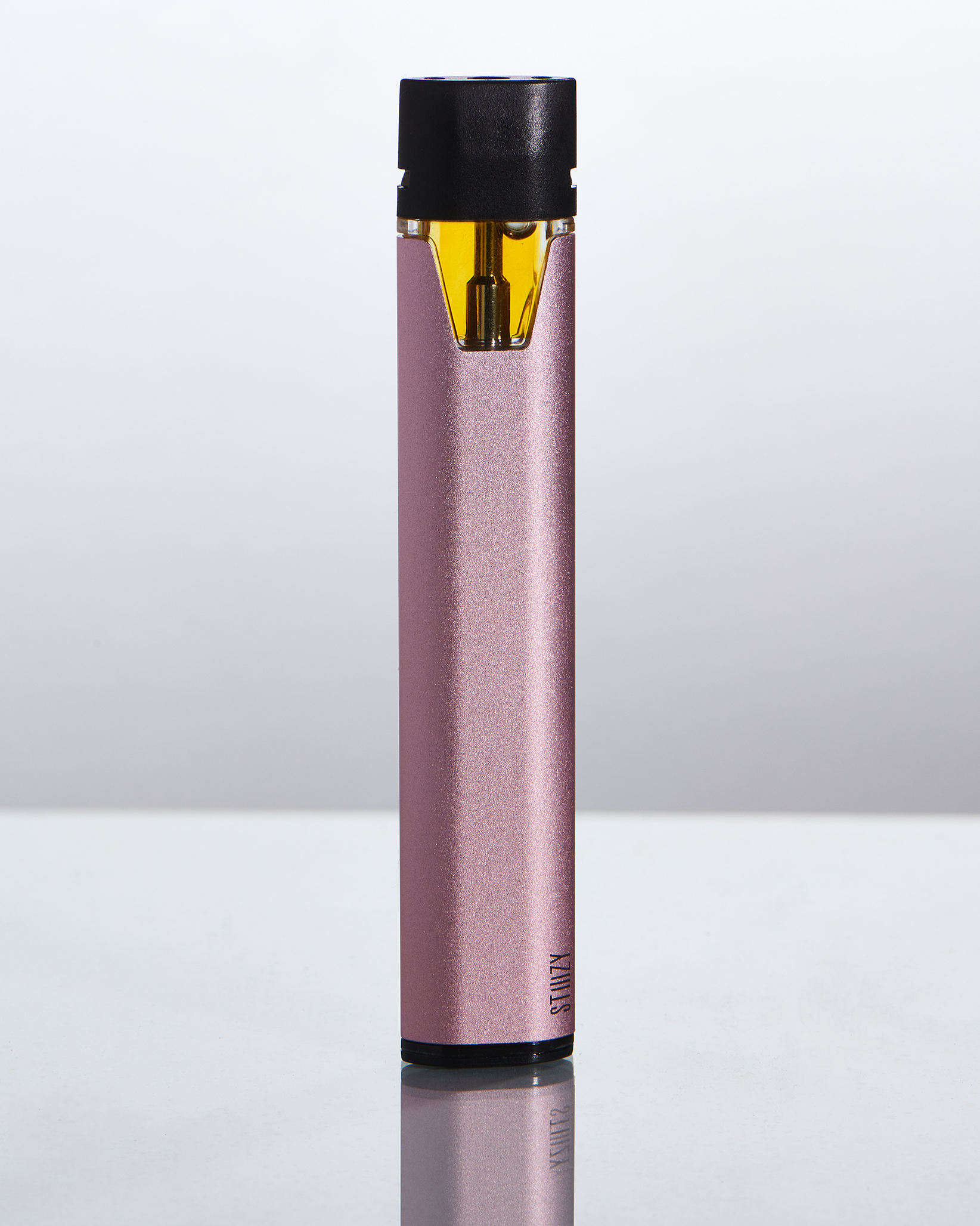 A rose-colored weed pen battery with a weed vape pod prefilled with cannabis oils stands on a gray surface.