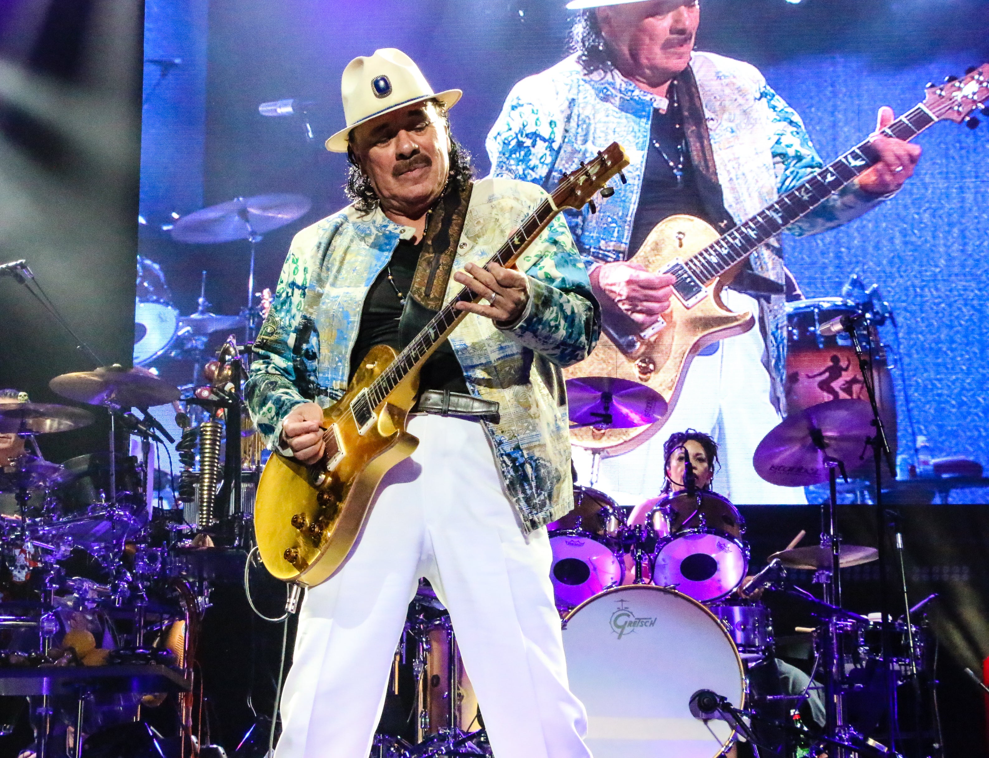 Cannabis flower loving celebrity Santana plays his yellow guitar on stage with his band.