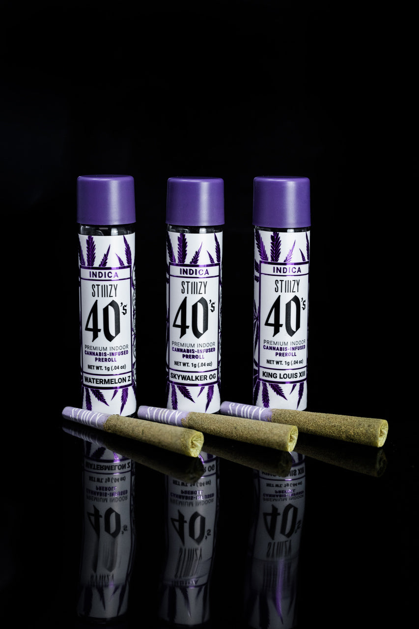 Three infused cannabis pre-rolls of an indica strain lie in front of their purple-capped jars.