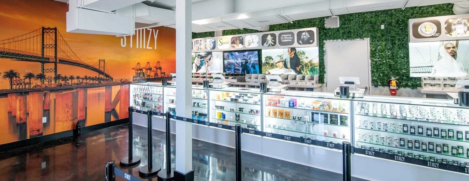 A weed dispensary with an orange painting of a bridge on the wall sells cannabis product in its glass counters.