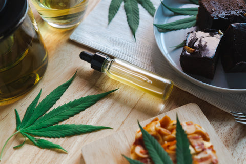 A tincture of cannabis oil sits on a table with different weed edibles.