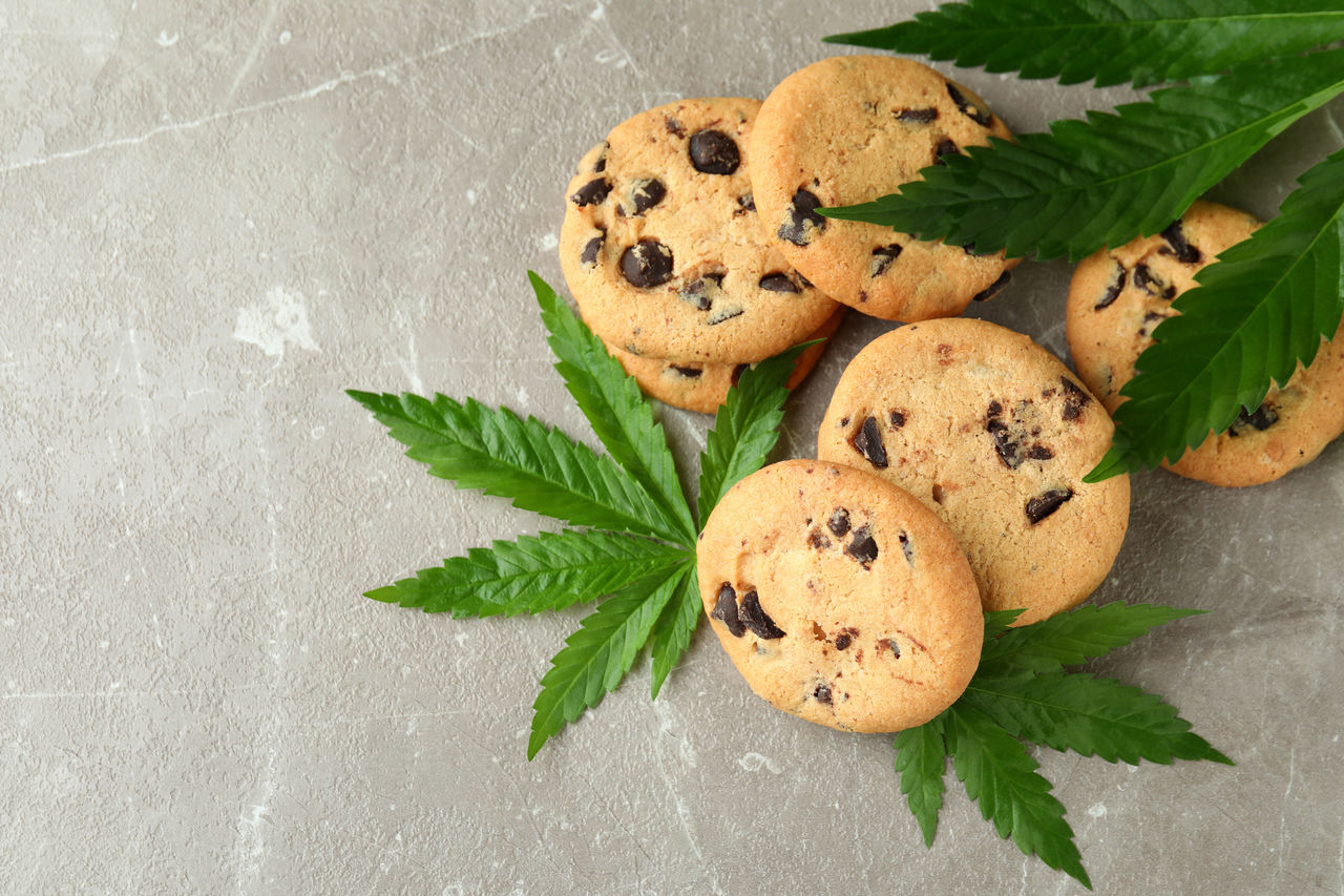 Cookie weed edibles piled on a gray textured table with cannabis flower leaves.