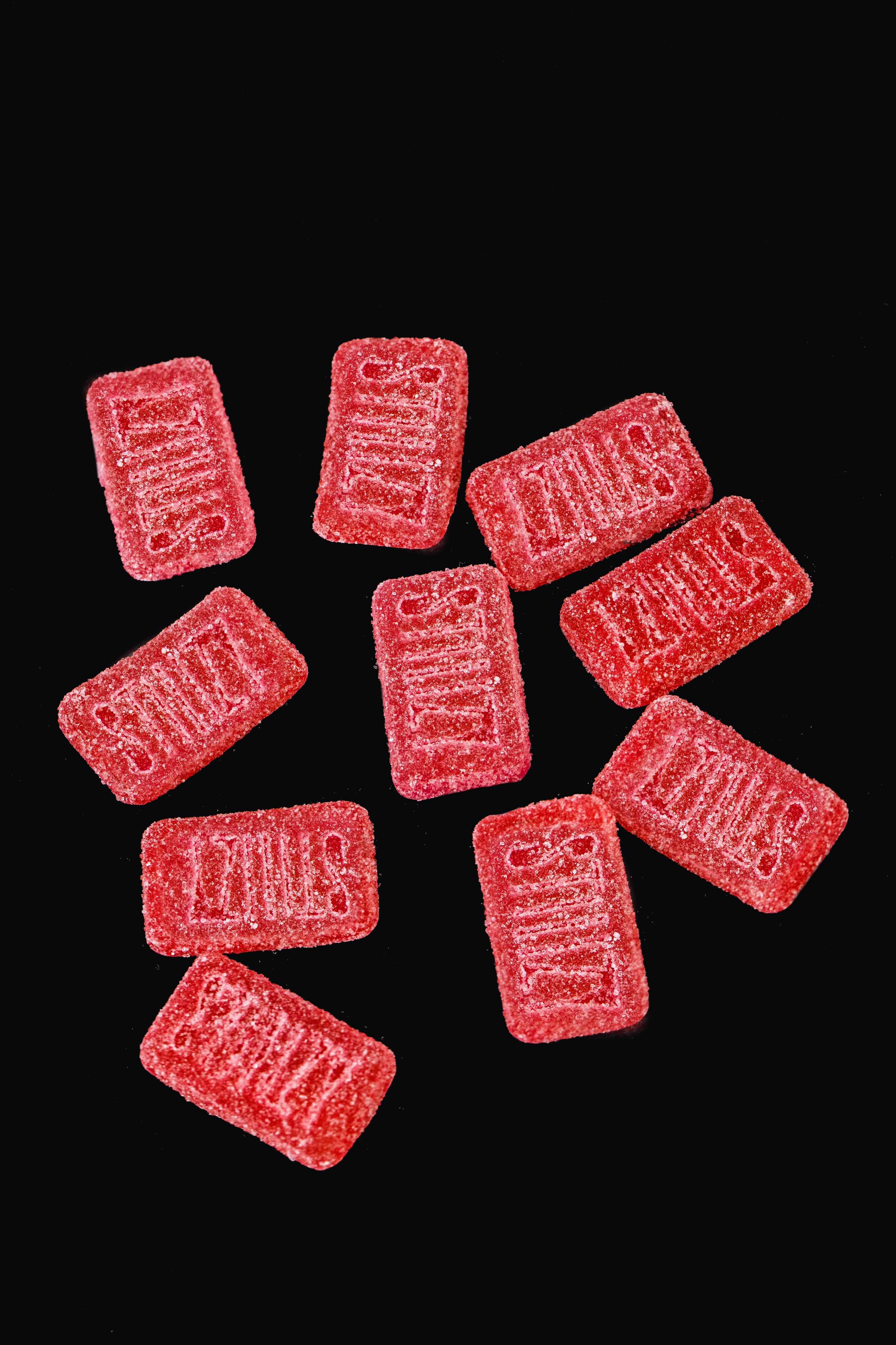 A cluster of bright neon red weed gummies from STIIIZY is spread out over a black background.