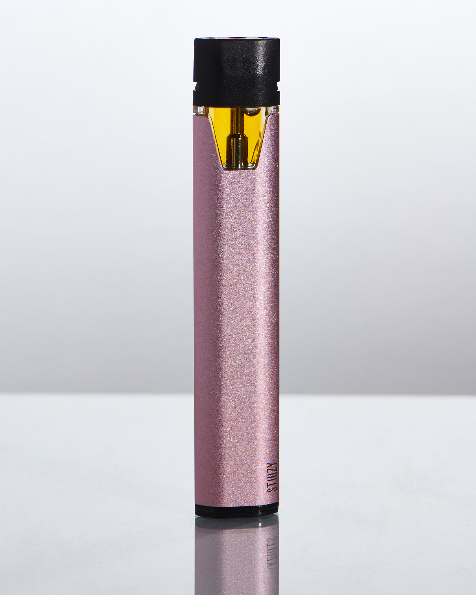 A rose-colored weed pen with its own vape pod and battery stands upright on a silver surface.