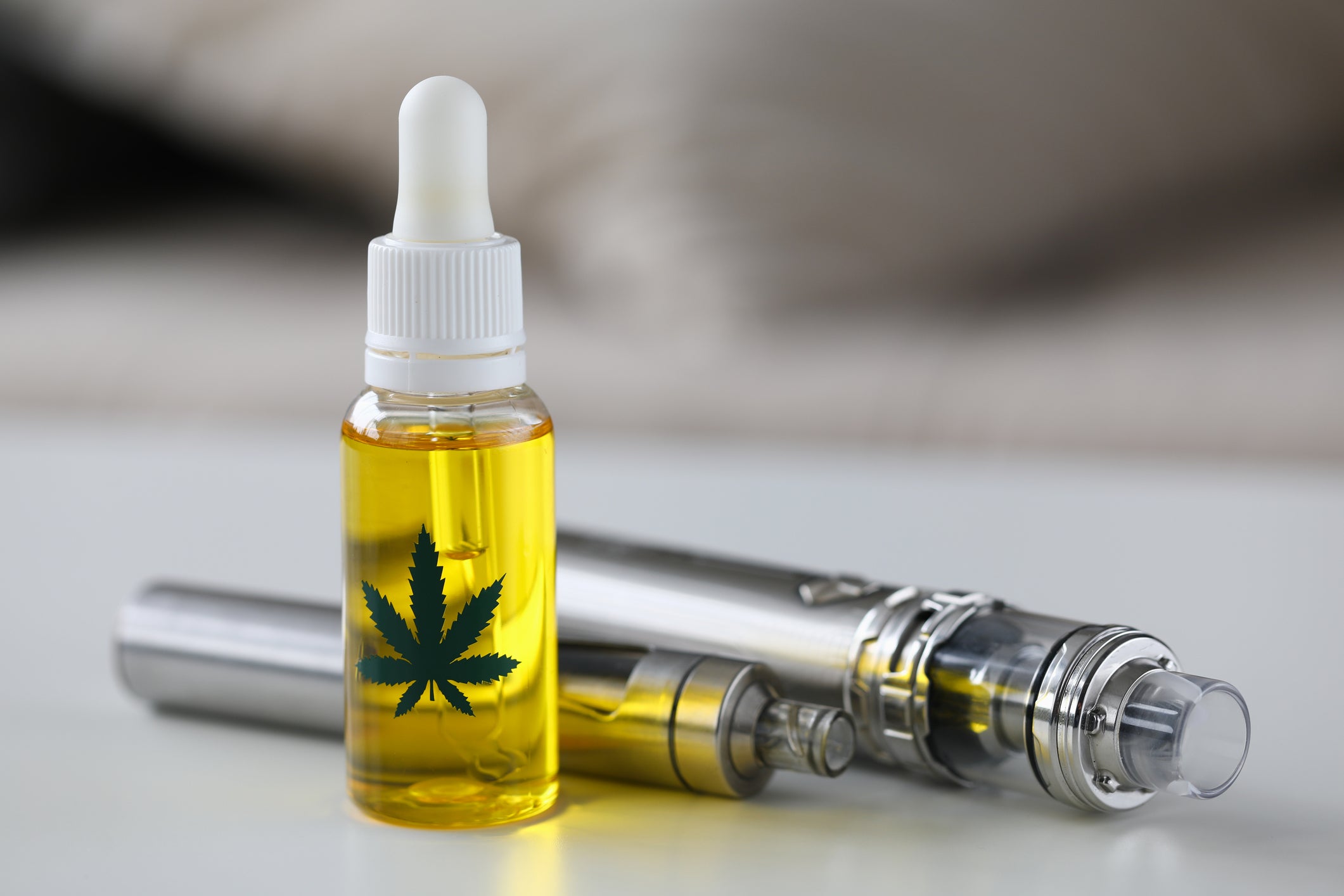 A weed pen with its vape cartridge lies next to a vial with cannabis distillate.