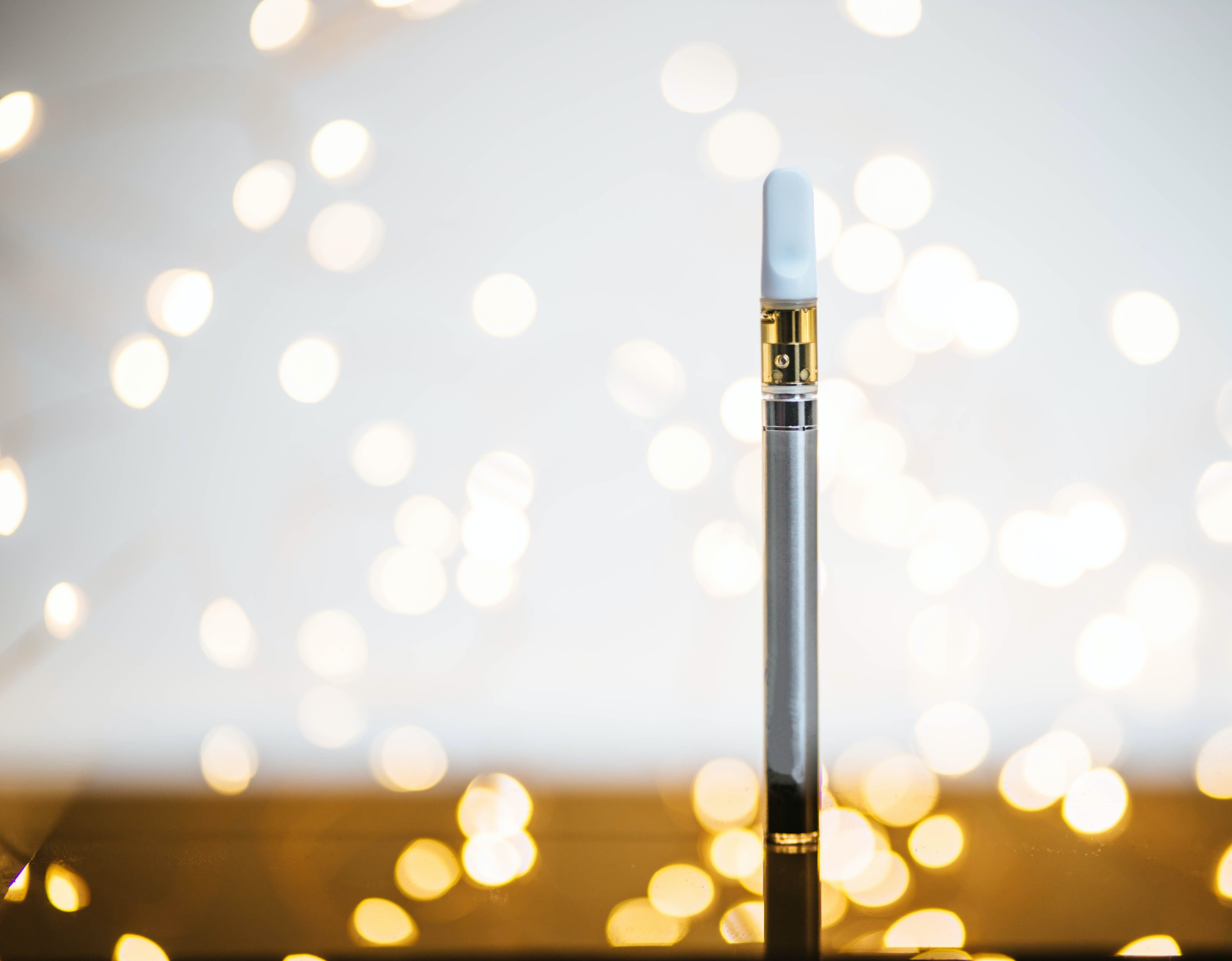 A weed pen with its white weed vape pod attached stands on a table amidst sparkles.