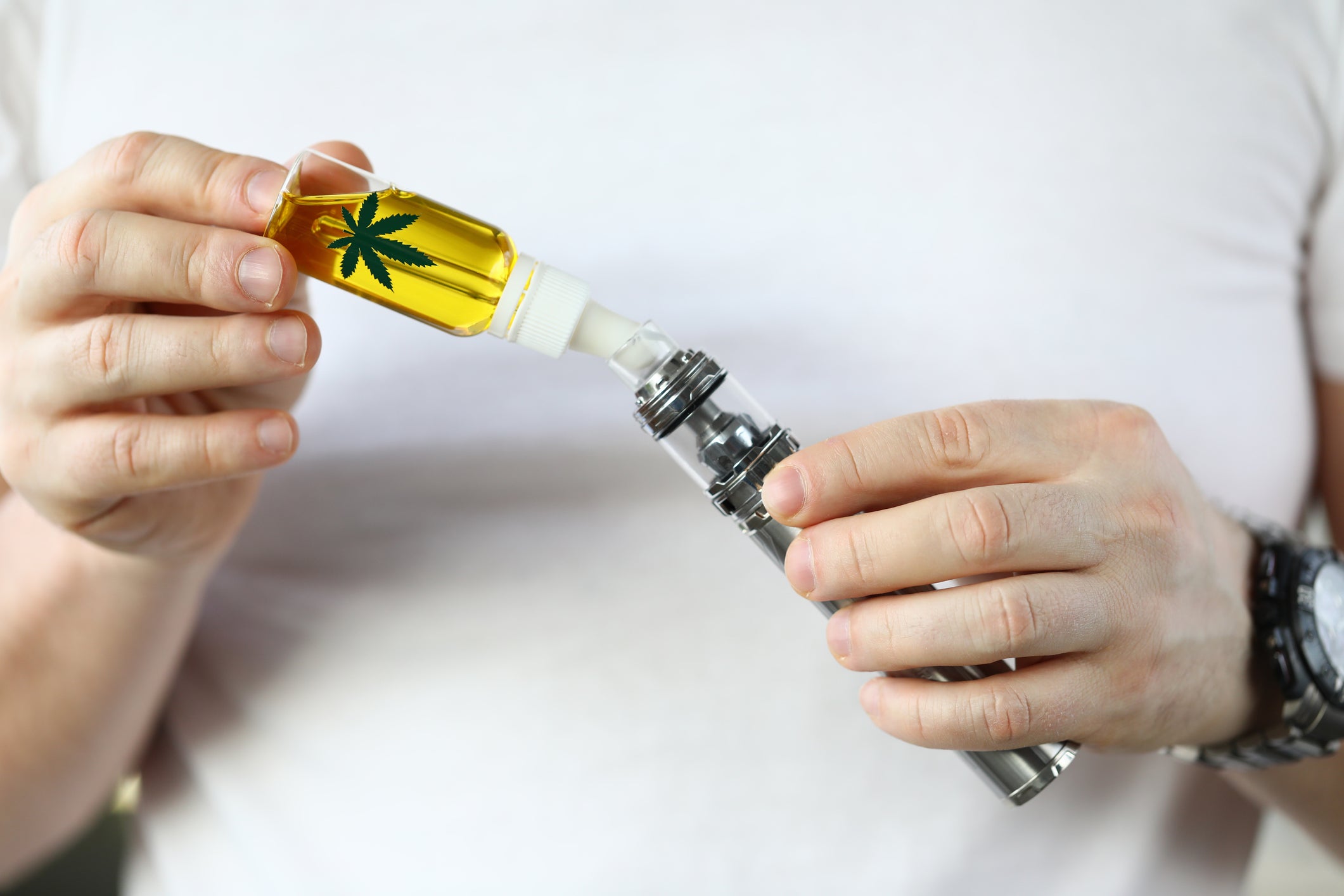 A person fills up a cannabis vape or dab pen with cannabis THC oil housed in a vial with the cannabis flower on it.