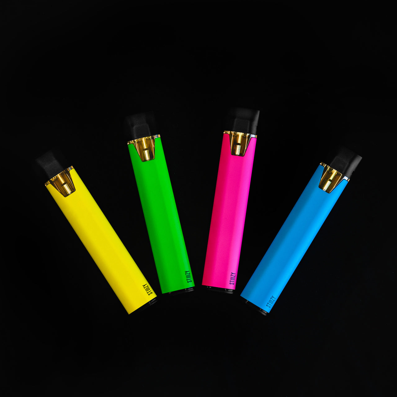A yellow, green, pink, and blue STIIIZy weed vape pen with THC distillate are spread out over a black surface.