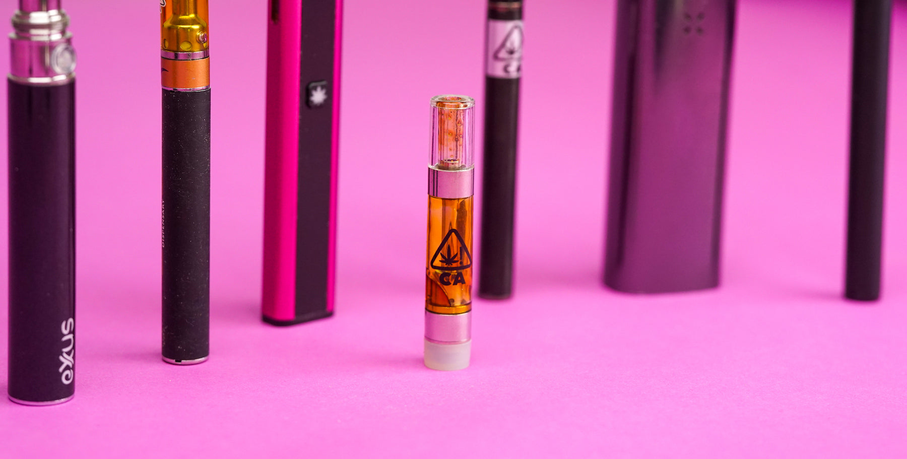 close up of a cannabis vape cartridge with an arrary of current portable vape devices in the background
