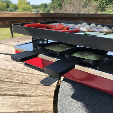 Raclette cheese melting under the raclette grill while bacon and vegetables grill on top