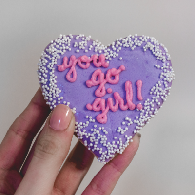 Purple heart-shaped cookie with the words "You Go Girl" iced on it