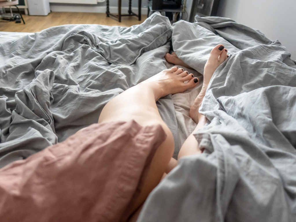 Woman in bed kicking her legs out from under her duvet