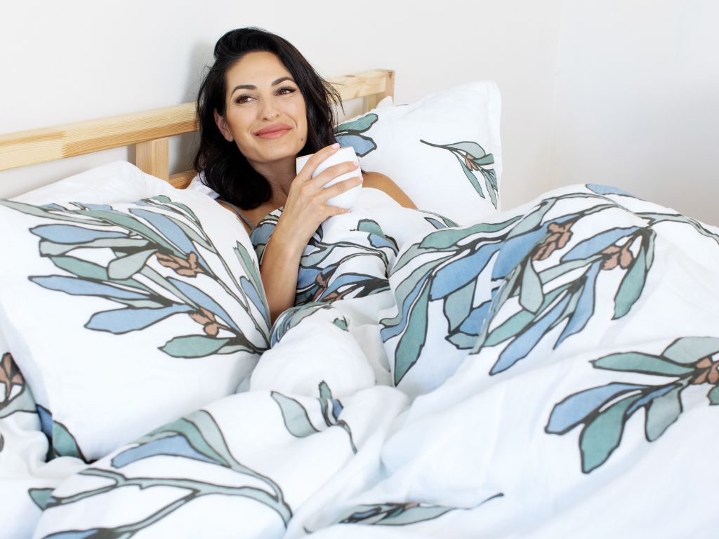 Woman enjoying a cup of tea in organic European flax linen bedding with botanical print by The Modern Dane