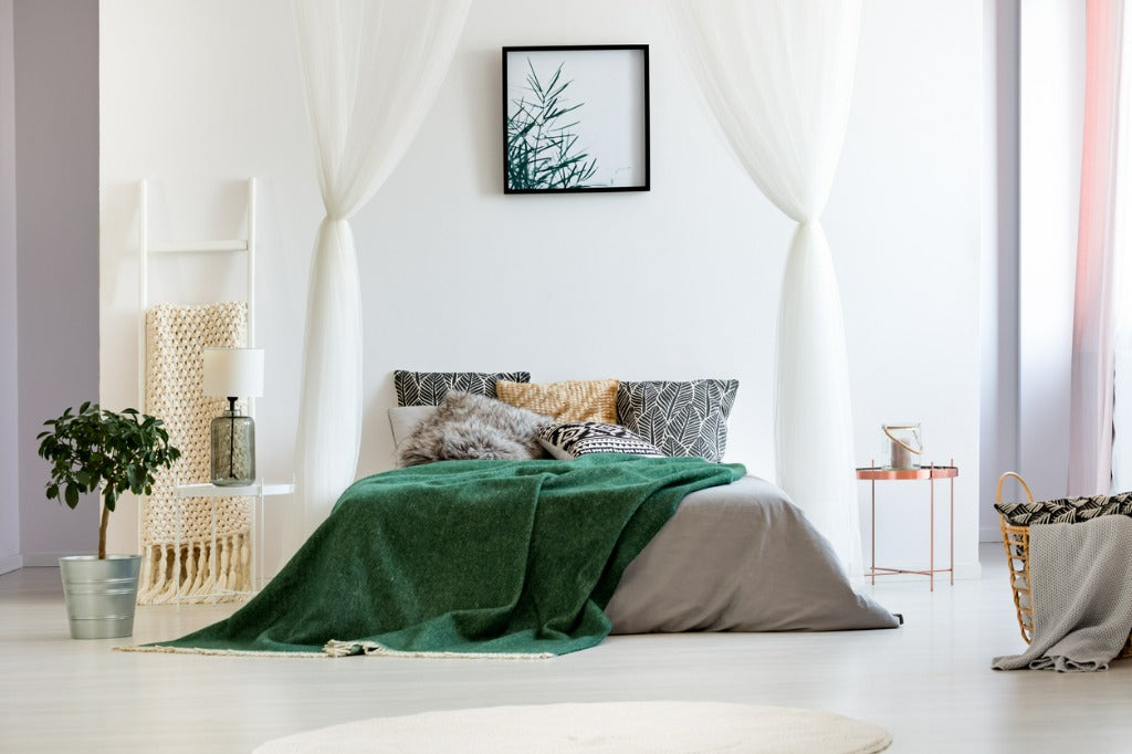 Copper nightstand and ladder blanket rack next to big bed with green quilt in white bedroom of spacious apartment