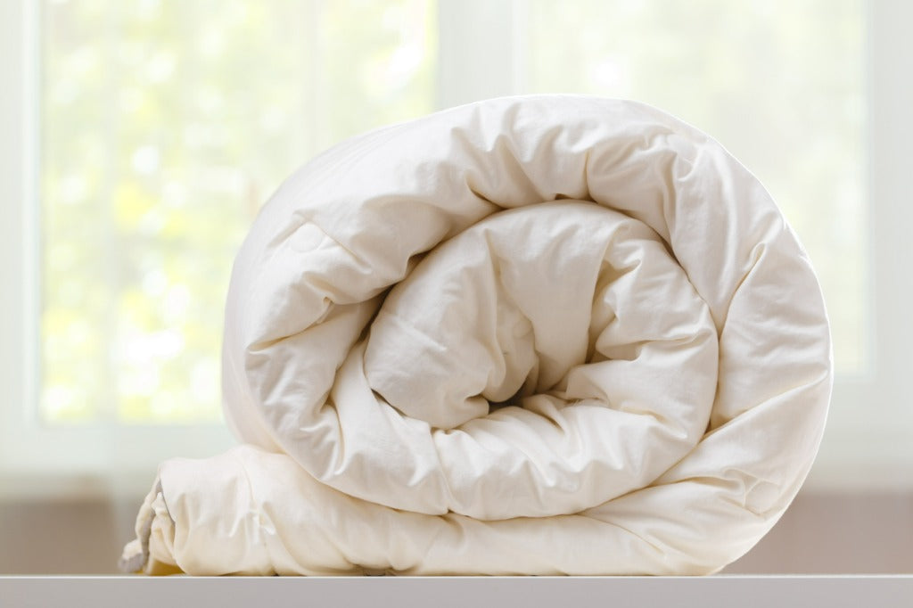 A folded rolls duvet is lying on the dresser against the background of a blurred window