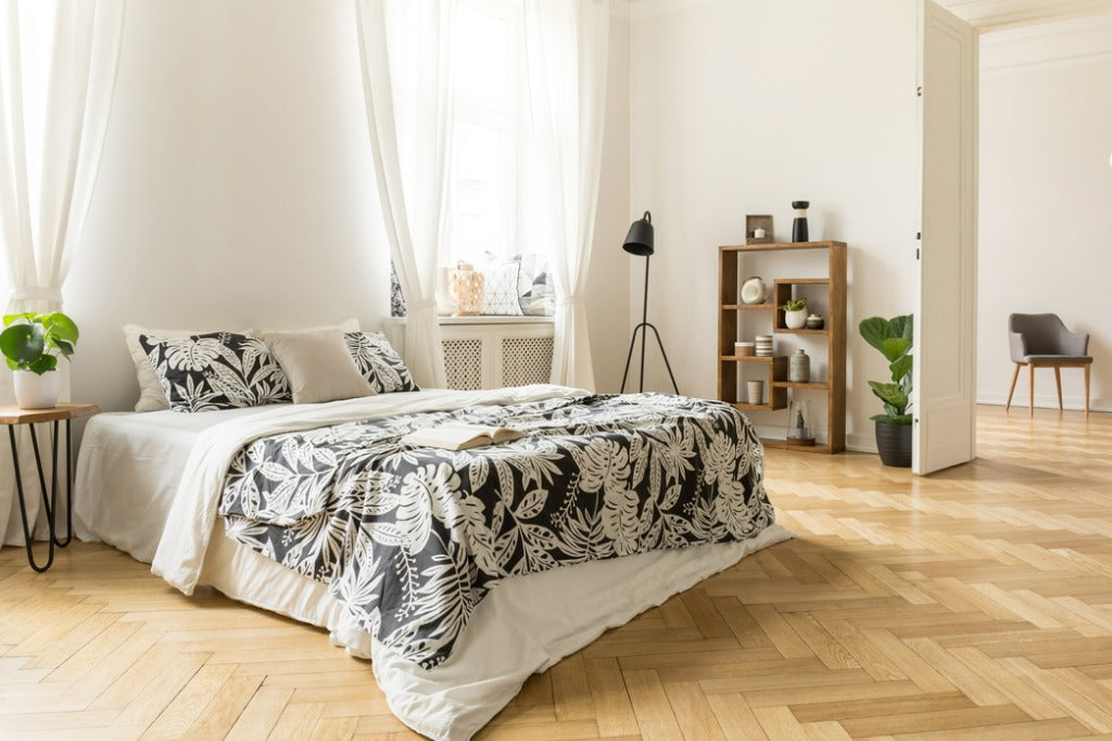 Stylish apartment interior with white walls and herringbone wooden floor. A view from a bedroom with a big bed to another room with an armchair. 