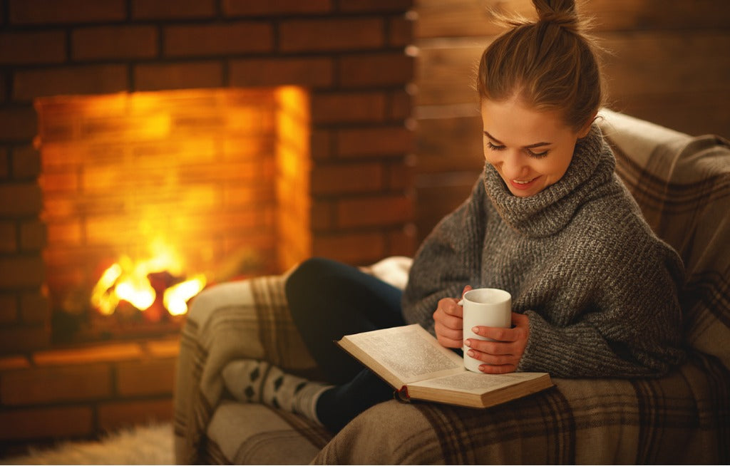 Young woman reading a book by the fireplace on a winter evening