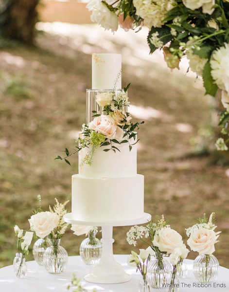 Wedding cake with white roses set on a table outdoors with roses in glass vases