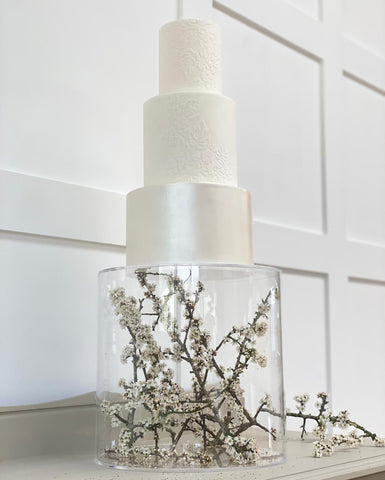 Floating cake stand using fillable acrylic cake tier containing whit flowers