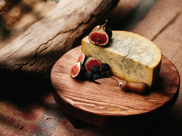 Tabla de quesos de madera oscura con queso azul y fruta.