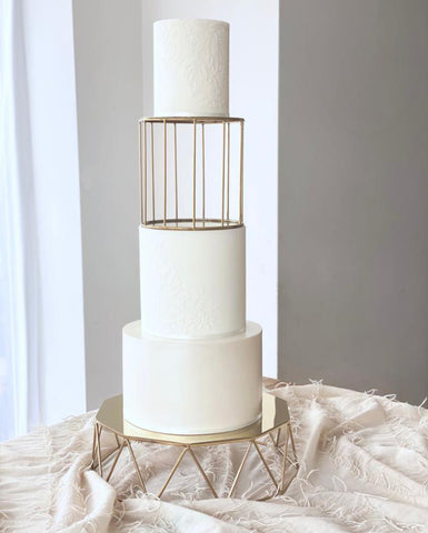 Pastel de bodas blanco de tres niveles con soporte para pastel dorado y separador de pastel tipo jaula para pájaros.