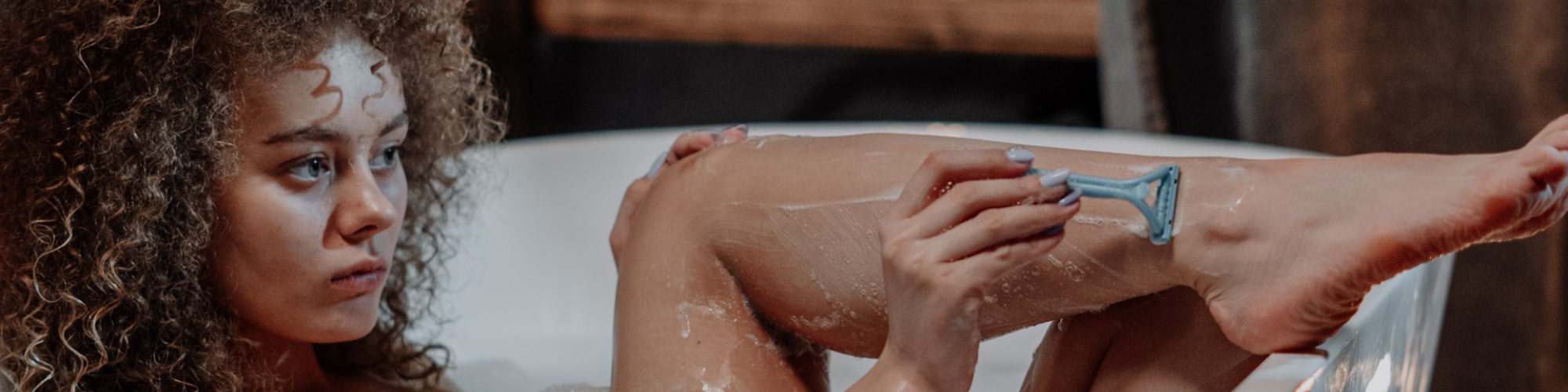Kvinde barberer sine ben med skraber i et badekar