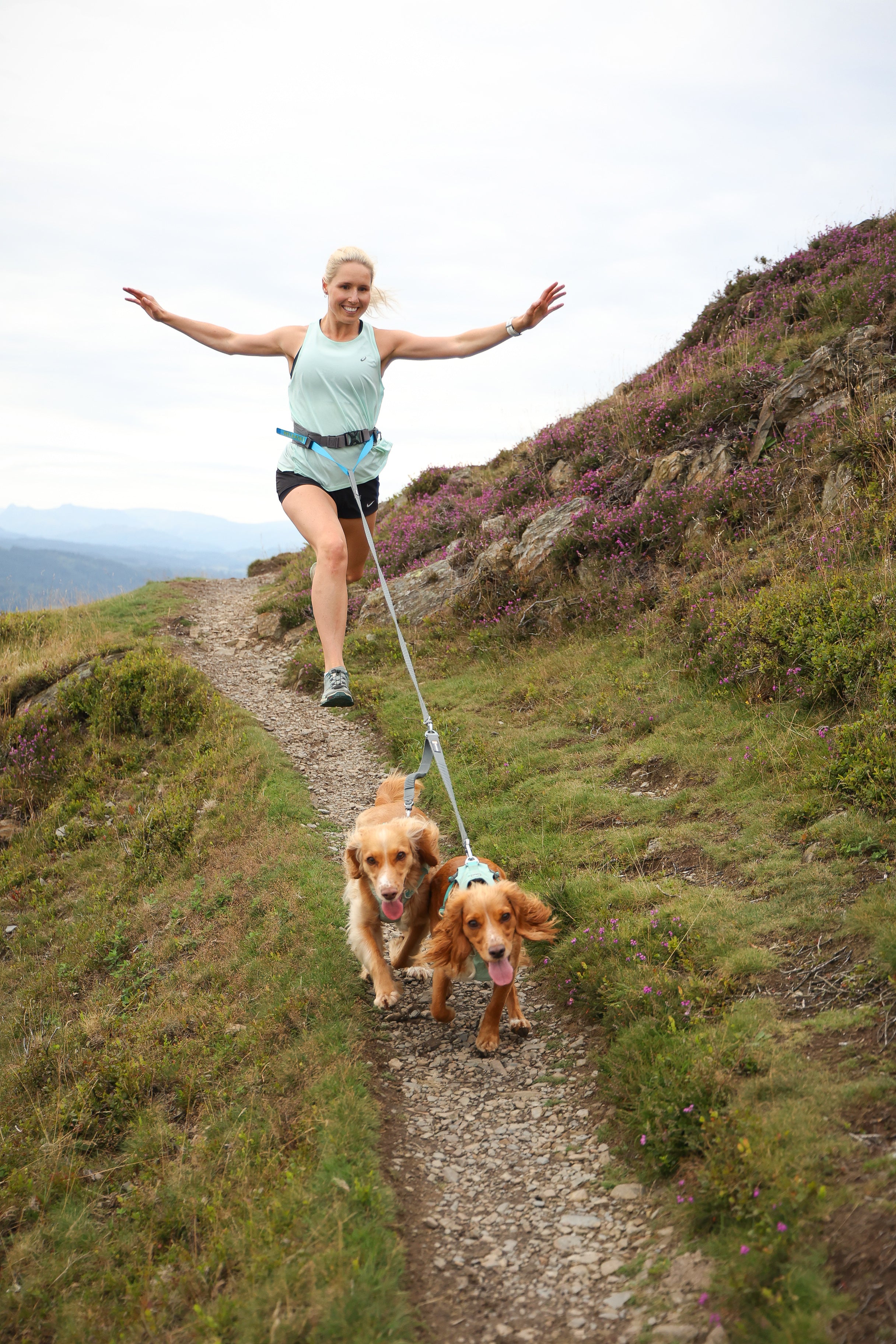 woman trail running with her dogs on leash and her arms outstretched