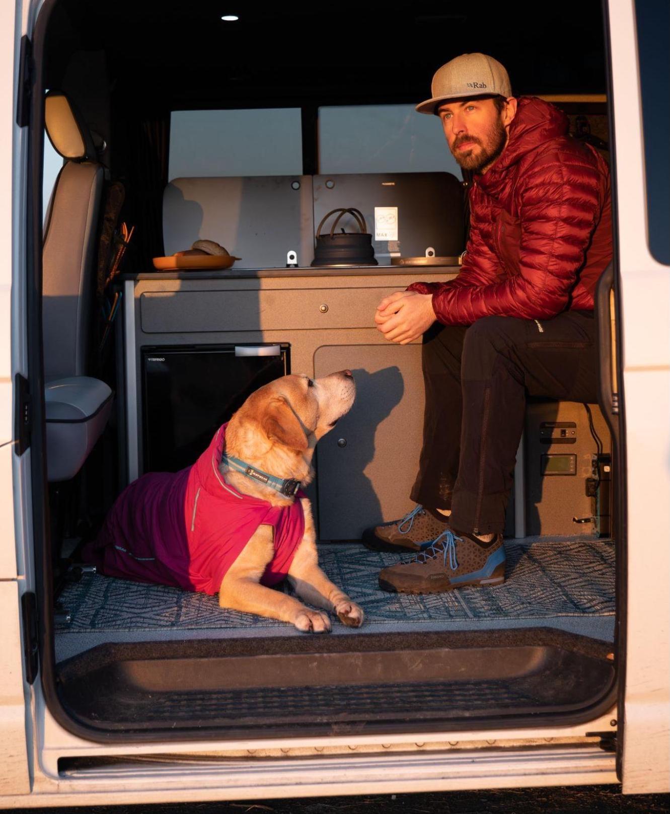 A man sits in a camper van with his dog.