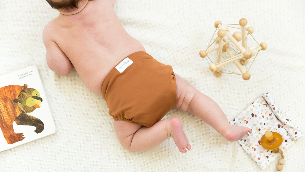 Baby crawling on floor surrounded by toys wearing a burnt orange Esembly Cloth Diaper