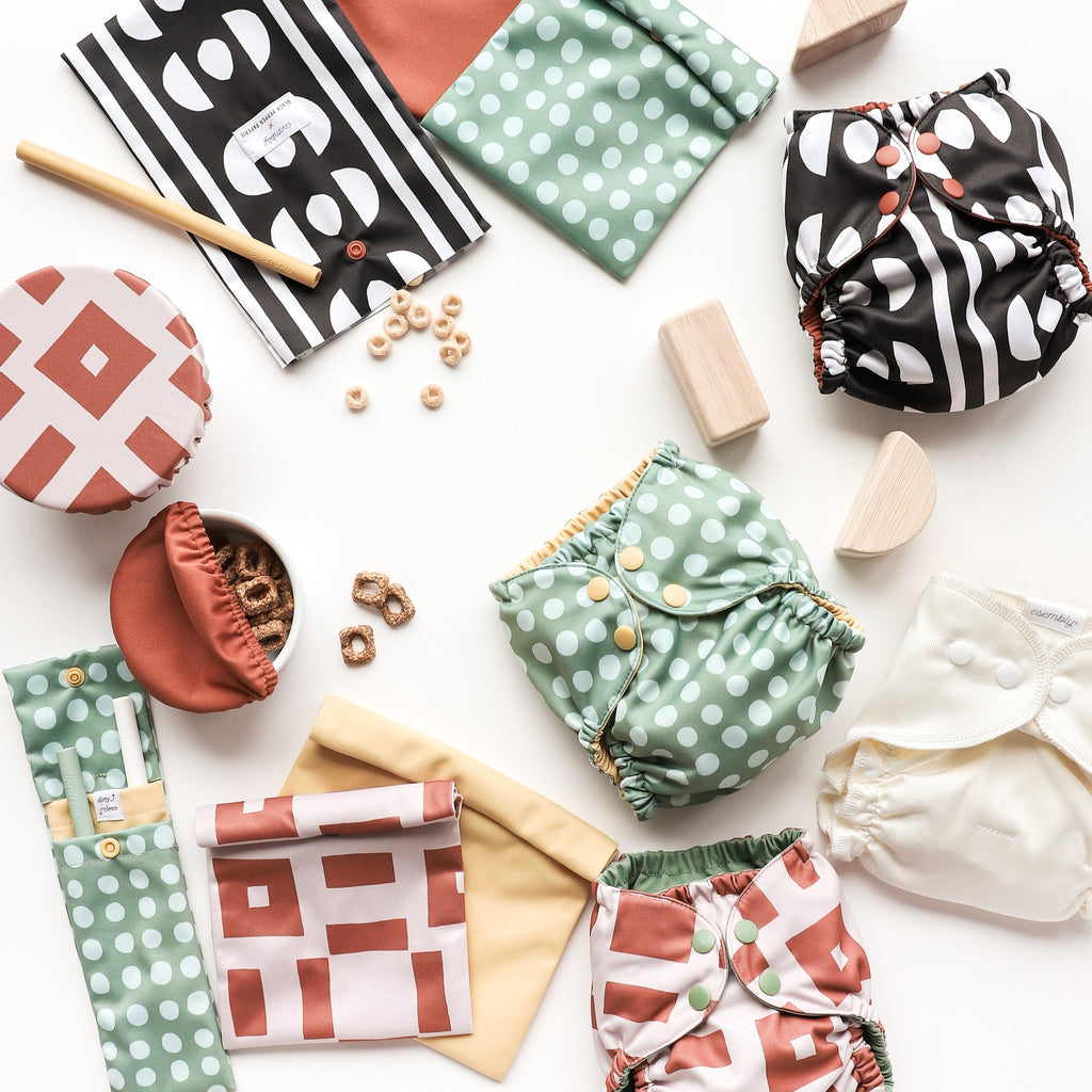 Image of the entire Black Pepper Paperie x Esembly collection including the Sipper Set, bowl caps, Outer Cloth Diapers, Reusable Food Storage Bags in brightly colored geometric patterns