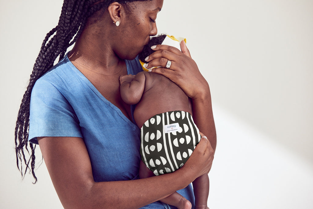 Woman in a blue dress holding baby in an Esembly Outer in Circuit (a black and white pattern with a half circle and organic circle pattern)