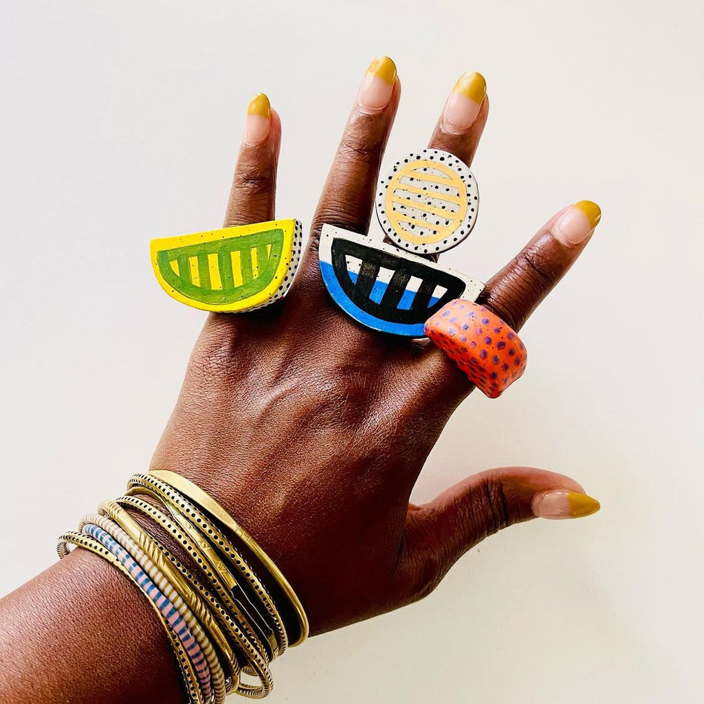 a woman's hand with colorful ceramic rings and gold and colorful metal bangle bracelets