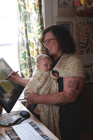 Illustrator Phoebe Wahl holding her baby while she draws