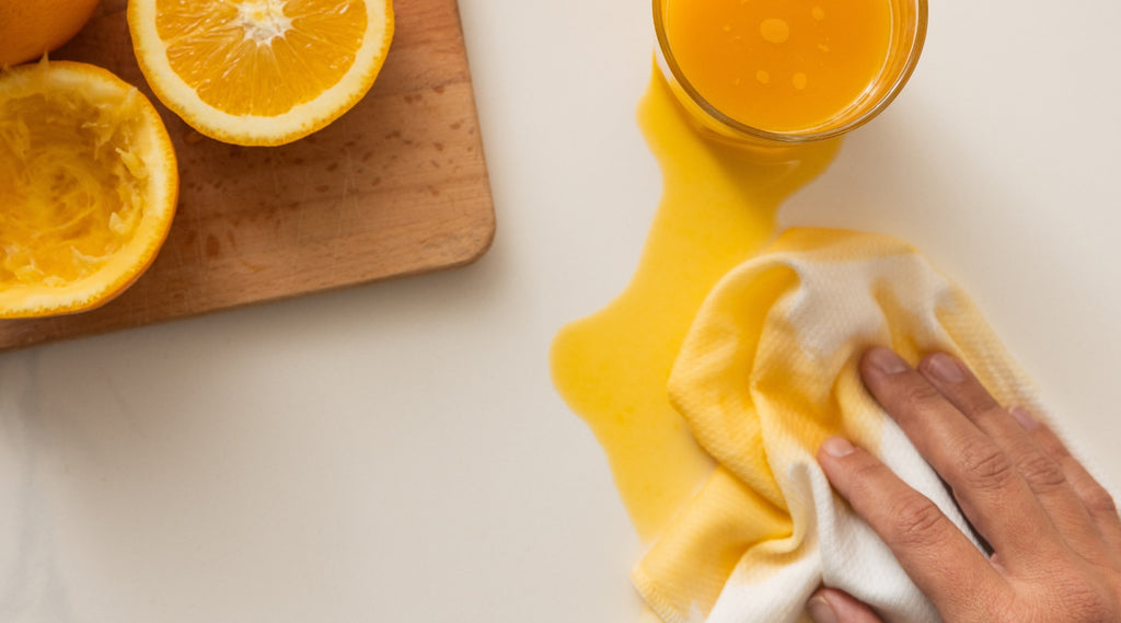 Sliced oranges on a cutting board and spilled orange juice from a glass being cleaned up by an Esembly paperless towel